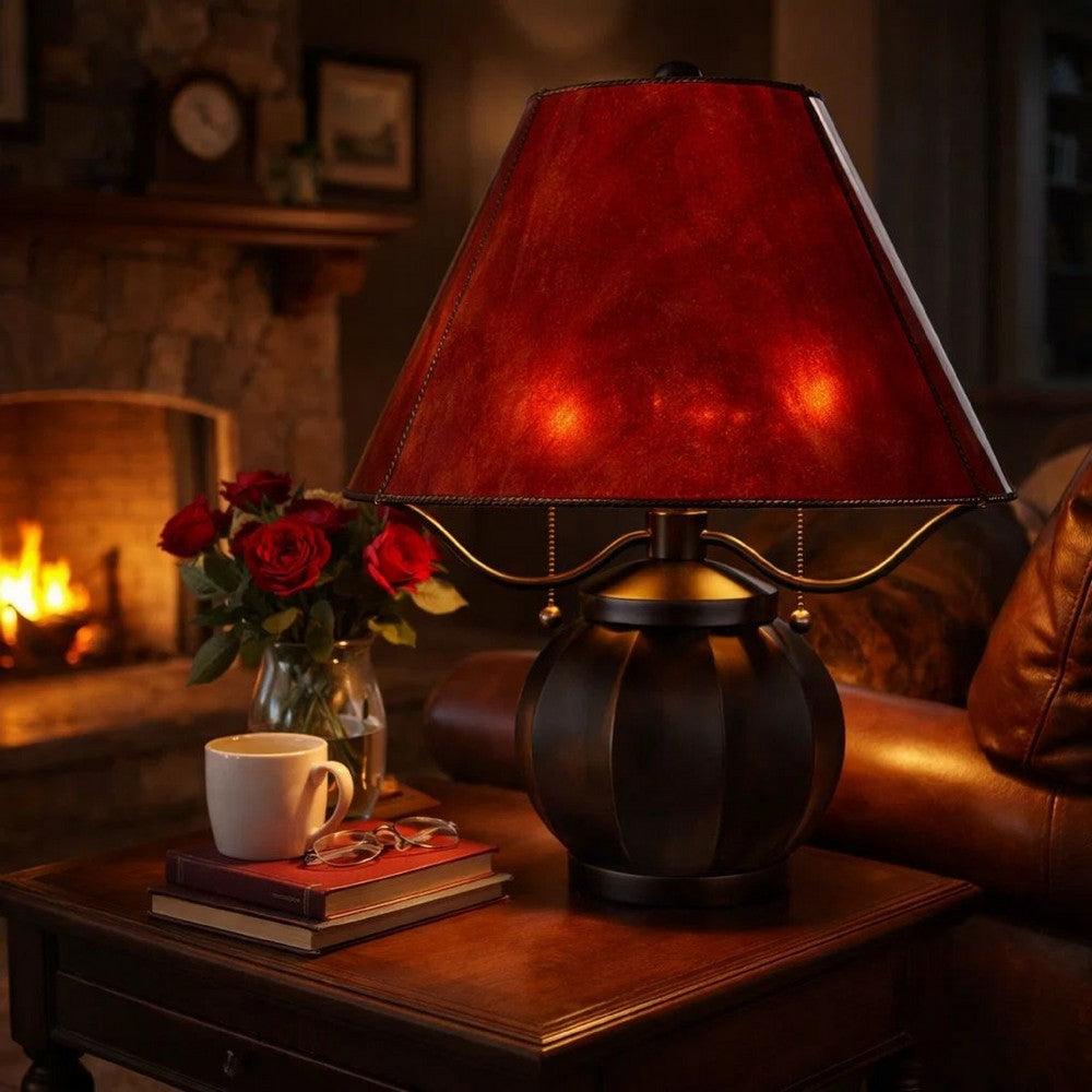 Dark red shaded table lamp glowing beside books with a fireplace behind